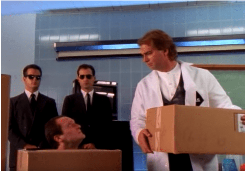 Image is a screenshot of Comedian Bill Engvall from his video titled "Here's your sign." Bill is holding a box, a man's head is sticking out of a moving box, and secret serviceman are behind the two men.